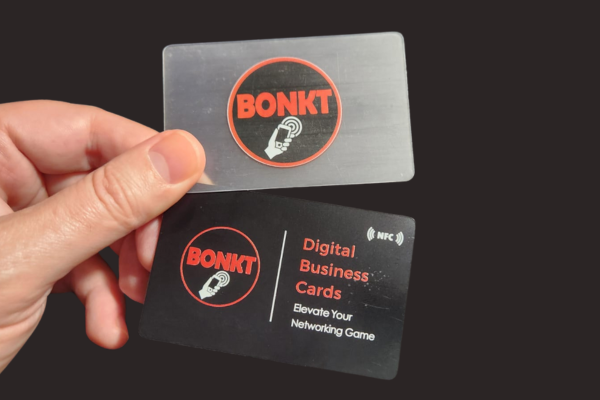 A hand holding 1 generic black coloured and generic clear BONKT NFC business card